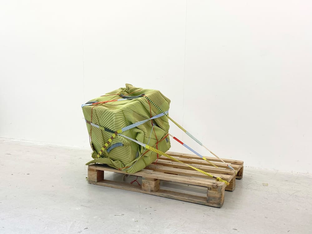 Wooden crate on the floor with a sqaure sculpture attached, sculpture created from textile materials