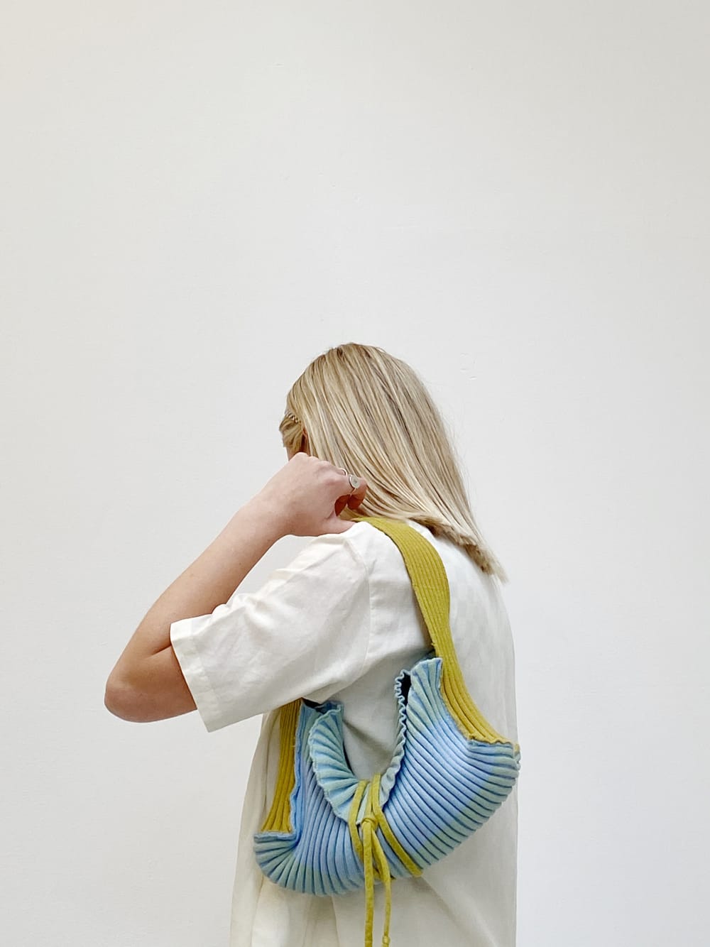 Female with blonde hair facing away from the camera, wearing a white t-shirt. Modelling the bundle bag which is made from yellow and blue material