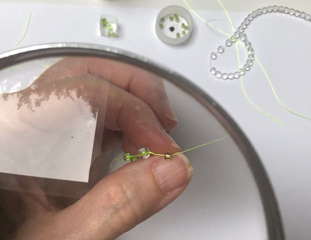 Hands holding a string of beads under a microscope