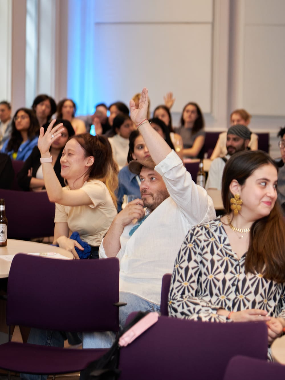 A shot of the audience attending the Alumni Ambassadors event, all in the photo have the hands raised and are laughing.