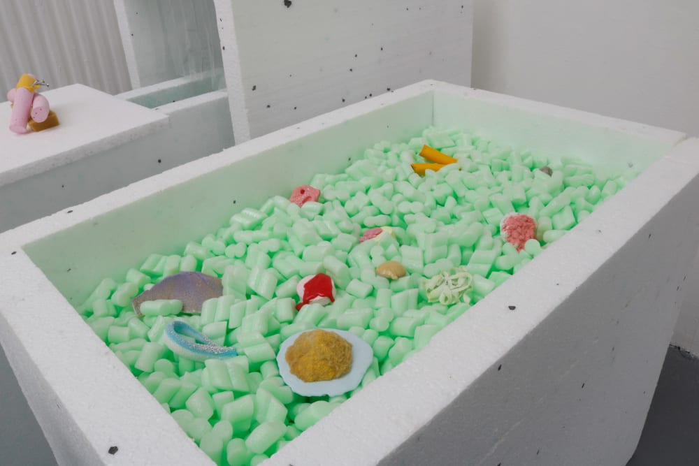  white container containing light green packing peanuts supporting a selection of small-scale sculptures