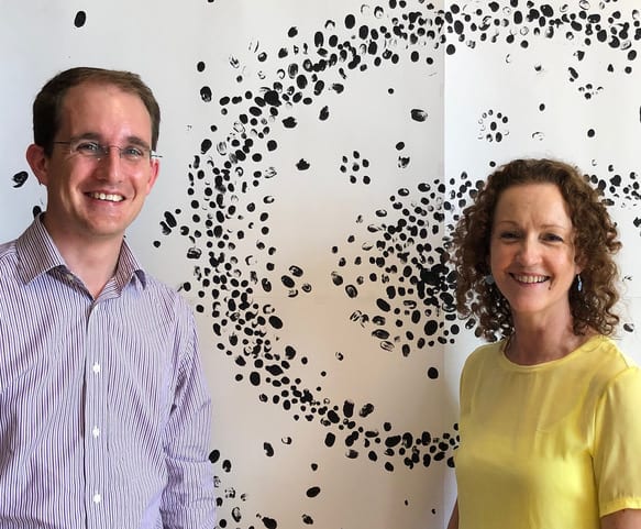 Two people stood smiling in front of a painting of fingerprints