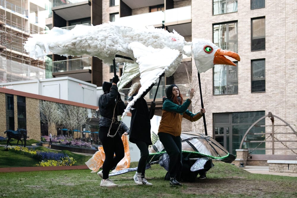 a seagull puppet seen from the side is operated by 3 people holding it above their heads.