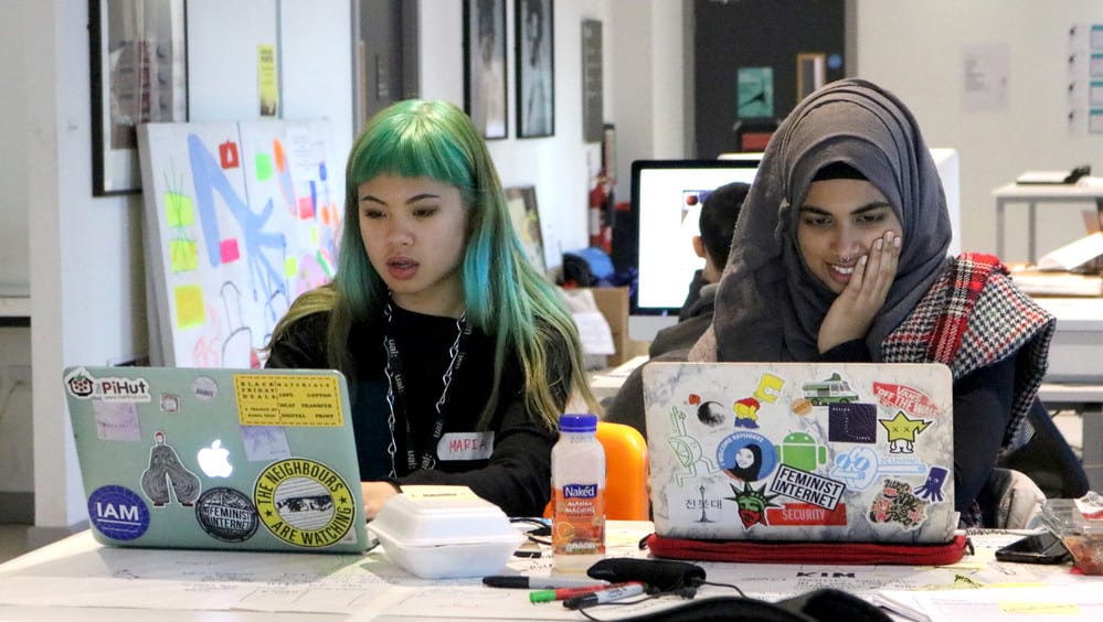 2 students working on laptops which are covered in stickers