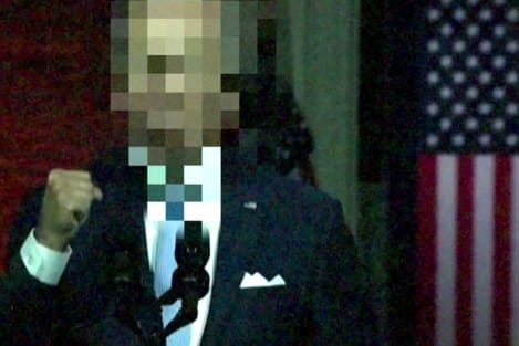A man in suit holds up his fist, his face is glitched. He's standing in front of the American flag.