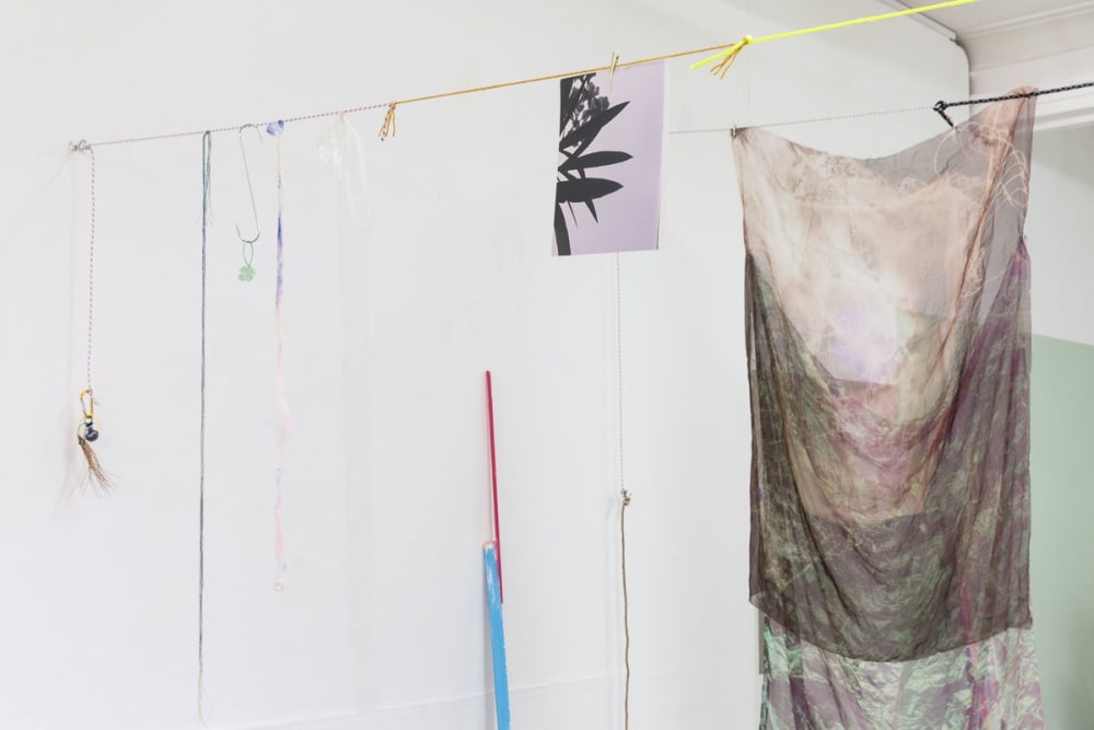 Fabric, netting, a photographic print and ropes are hung from a yellow string across a room.