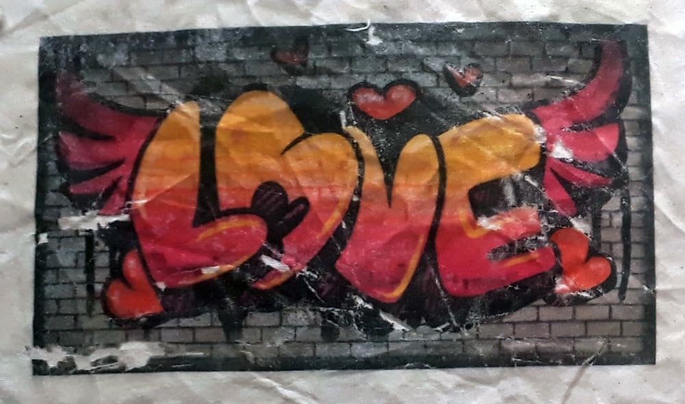a cartoon graffiti illustration of the word 'LOVE' in orange and red, painted on a grey brick wall