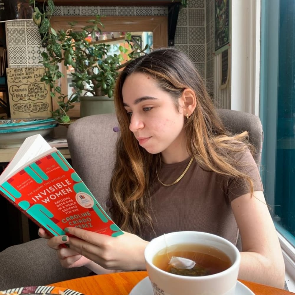 A woman with long hair reading a book called 'Invisible Women'