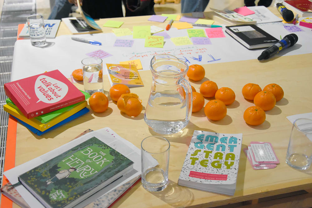 Close-up of a table at the Designing for Wellbeing event scatted with post-it notes, books, a water jug and glasses