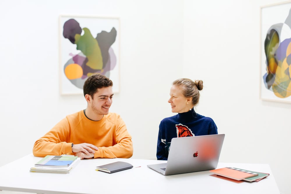 A student intern sat at a table with a colleague in a contemporary art gallery