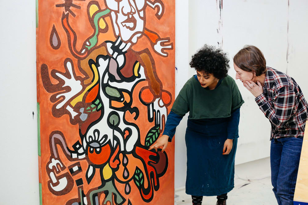 Two people leaning down to look at the bottom of a large, orange, black and white painting