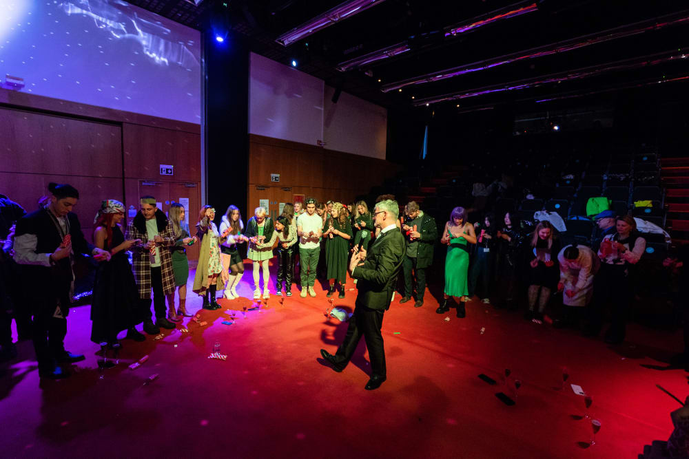 The host stands in the spot light with crowds surrounding him 