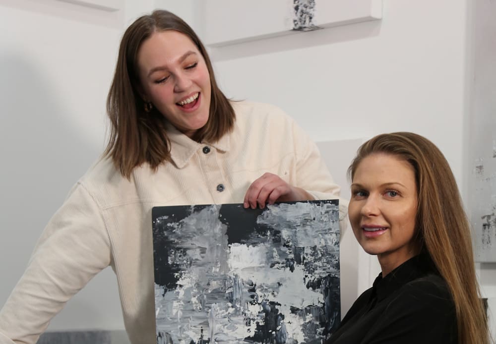Photograph of two women, one of whom is holding an acrylic painting.