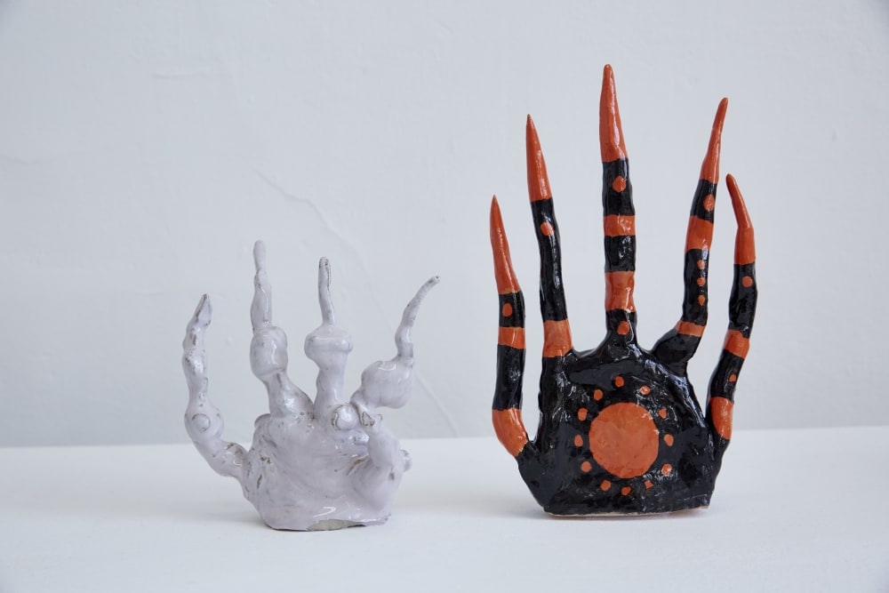 Image shows 2 ceramic sculptures – one white and one black and orange. They resemble hands, with long ‘fingers’ rising up towards the top of the image.