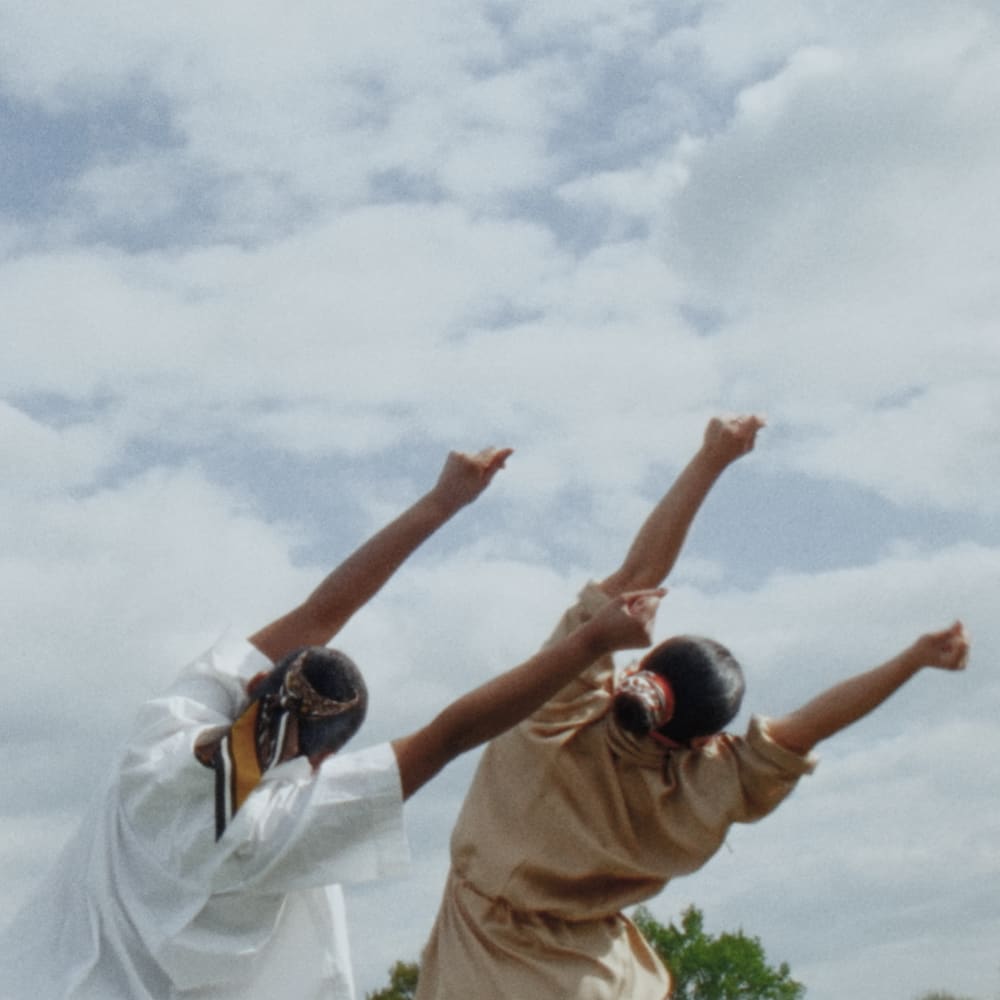 Still from 'Traces of Love' showing two people with their arms raised and back turned to the camera, swaying to the right