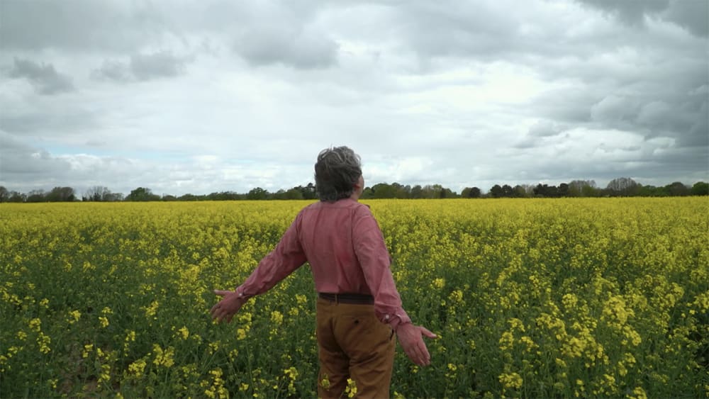 Film still of a naked man standing in a field.