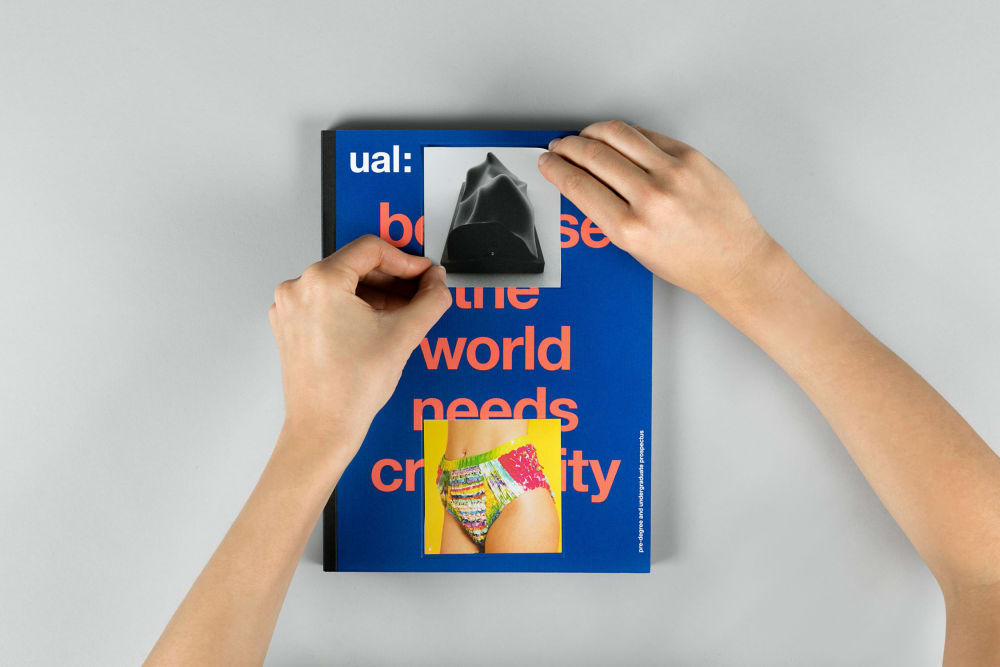Hands placing a second square sticker over the title of the 2018 undergraduate prospectus booklet, the placement of 2 stickers creates the brandmark on the cover of the prospectus.