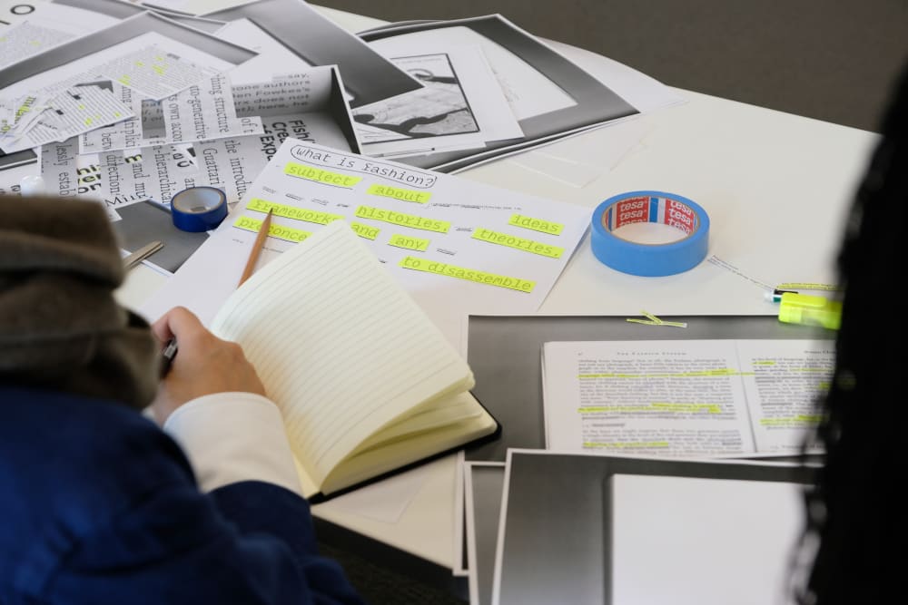 Paper and notebook on a table with a person's hand taking notes.