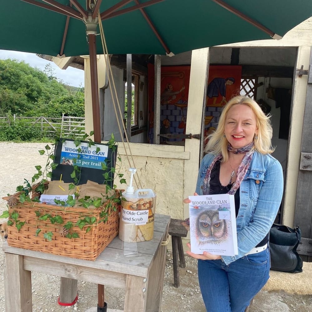 Photo of Annie in a blue jumper and blue jeans, holding a copy of her book