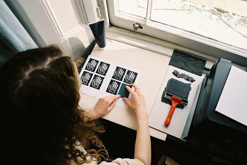 Cara Lloyd lino-printing a series of hand shapes from above the shoulder