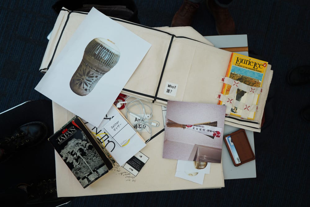 A collection of images, books, headphones and a card wallet seen in a pile on a table from above.