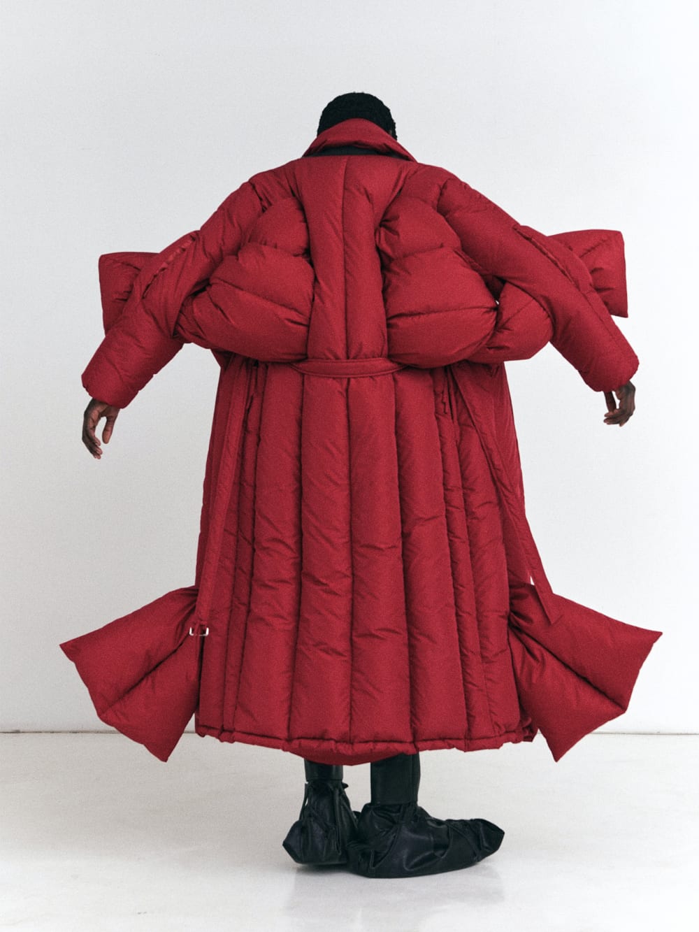 Back shot of model wearing Red Multi Slit Plaited Puffer Long Coat