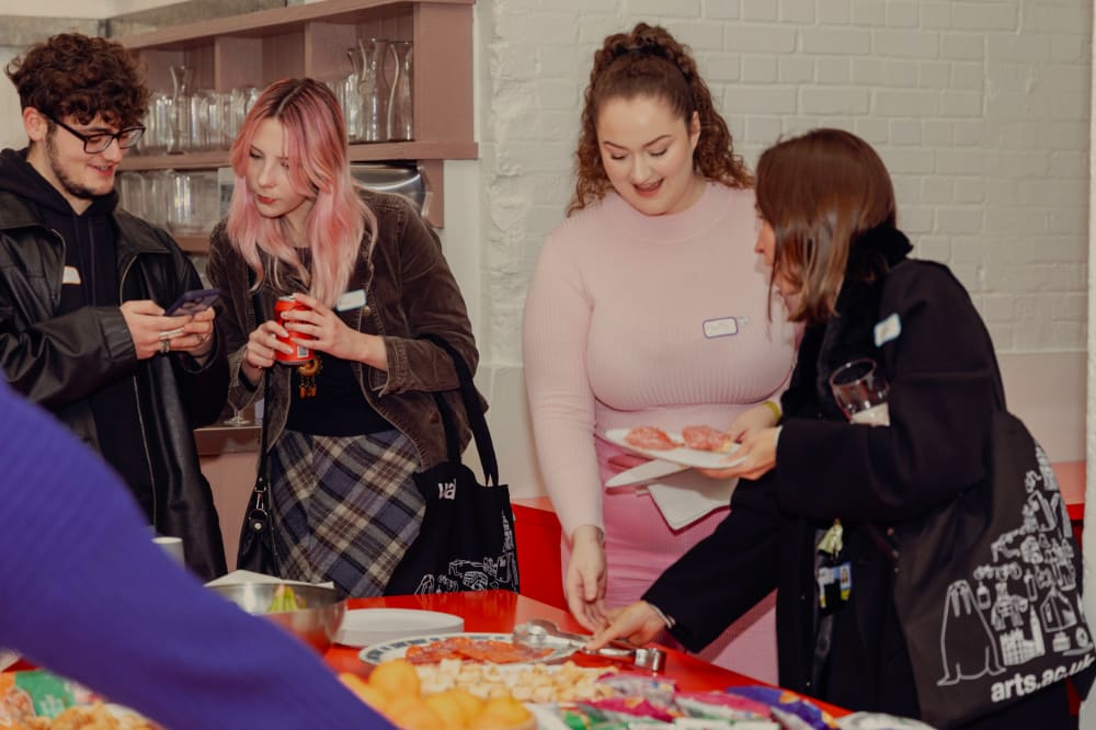 A group of people getting snacks around a table and talking.