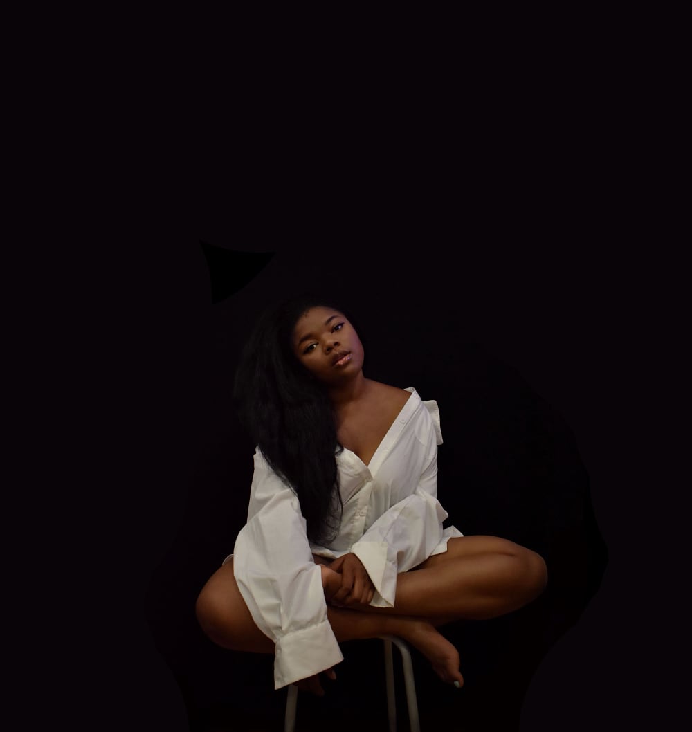 Savanna sits crossed legged on a stall, wearing a white shirt, black backdrop