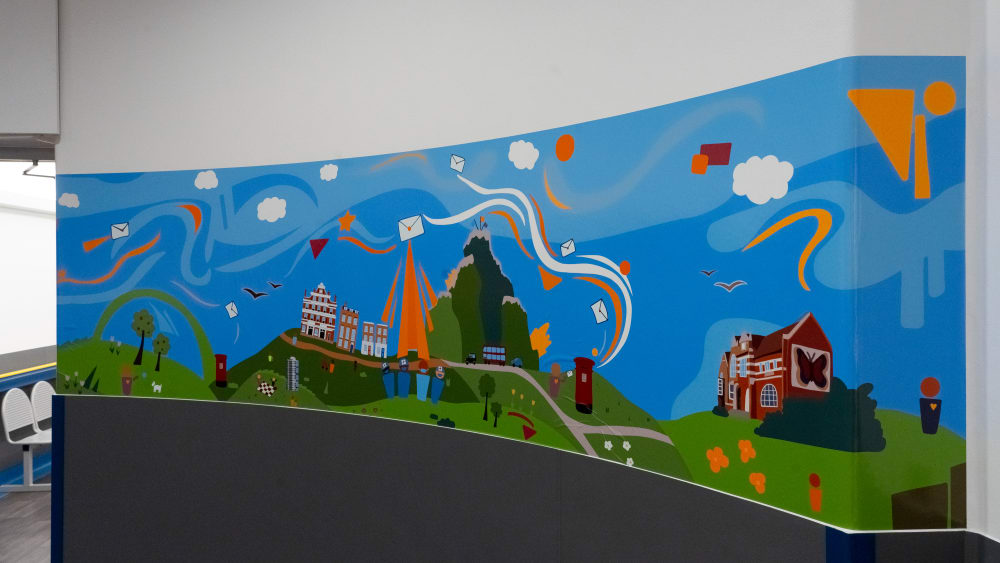 Image shows a colourful mural on a curved wall. In the background you can see a seat.