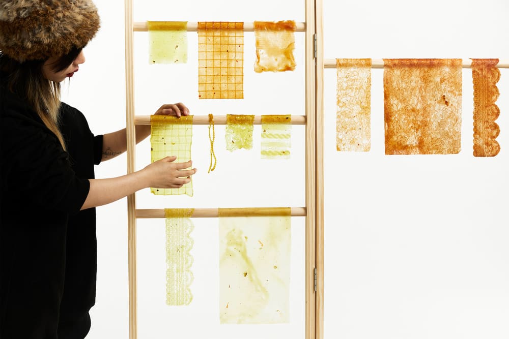 A collection of intricate textile samples that resemble lace hanging over a wooden structure.