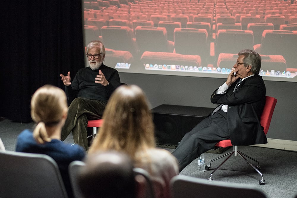 two men talking in front of a screen