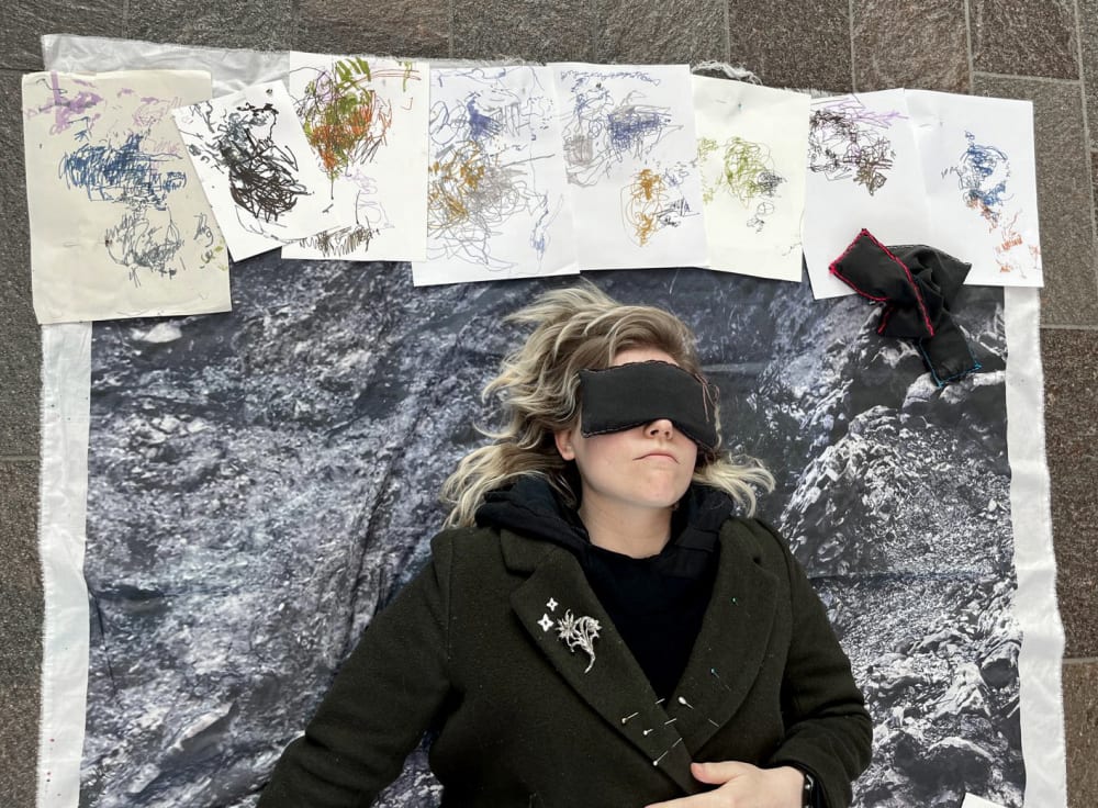 A person wearing an eye mask laying on the ground with a series of sketches above their head