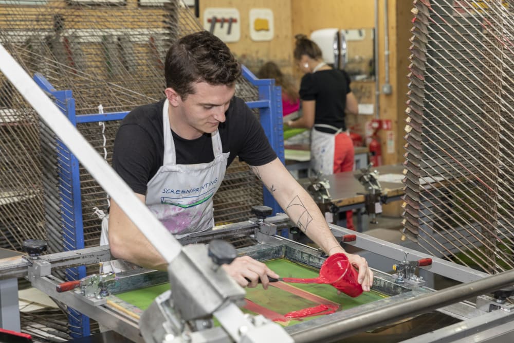 A student wearing an apron and printing a large-scale item
