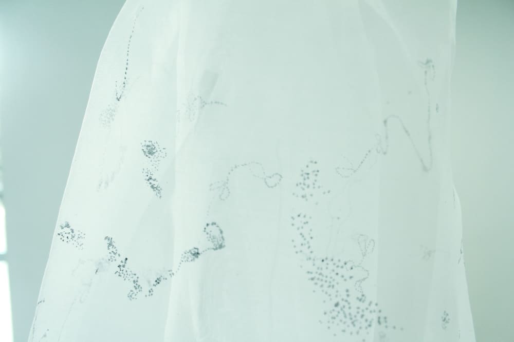 A close up image of some white fabric marked with dark grey and black abstract dotted images and lines