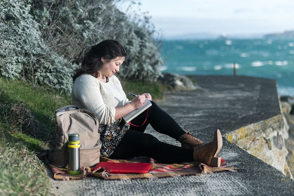 A woman writes on a clifftop.