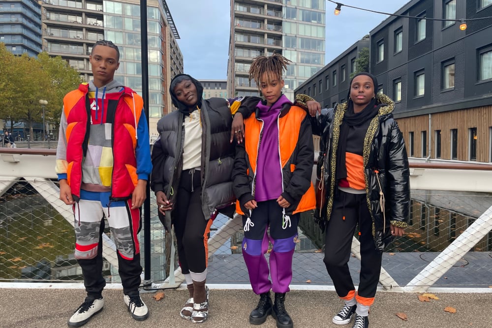 A group of four people wearing bright, colorful jackets and pants, smiling and posing together in a lively setting.
