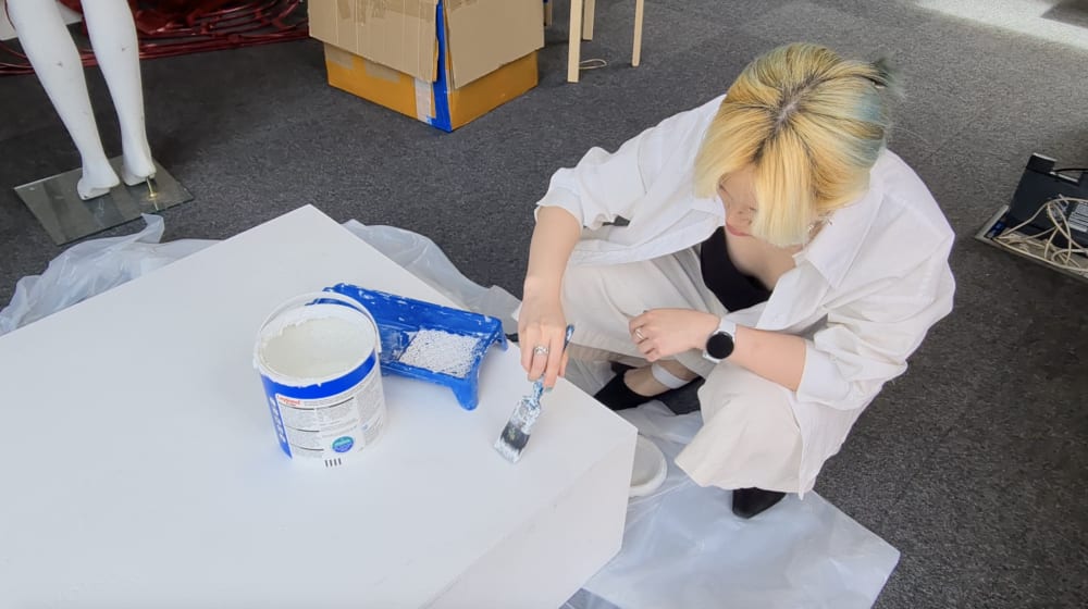 A person crouched over a table painting it white.