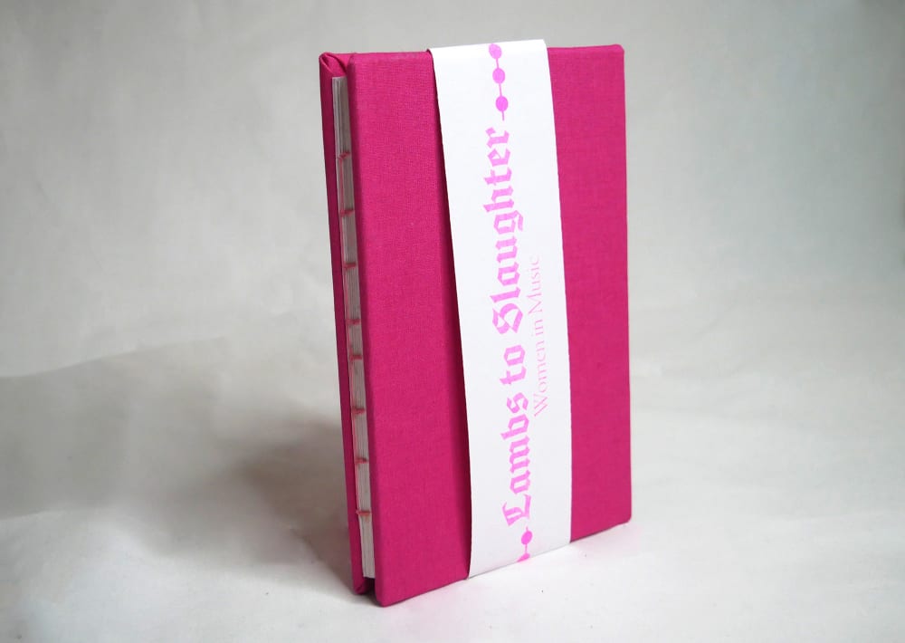 The publication is presented, a small pink book in hardcover. The title is printed upon a separate piece of paper in a faux-gothic typography and placed lengthways across the book. 