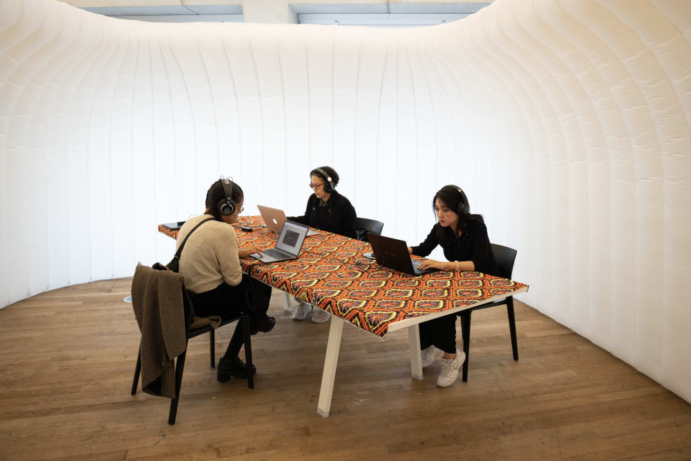 People wearing headphones and using laptops on a colourful table.