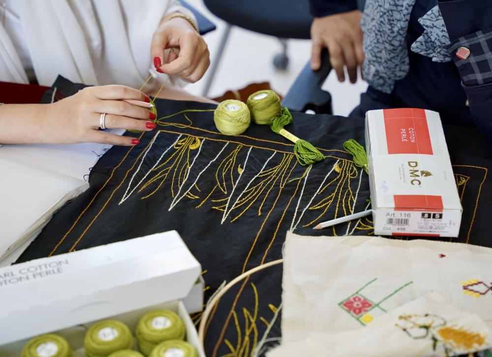 Two pairs of hands work on embroidery project (black, white and gold thread)
