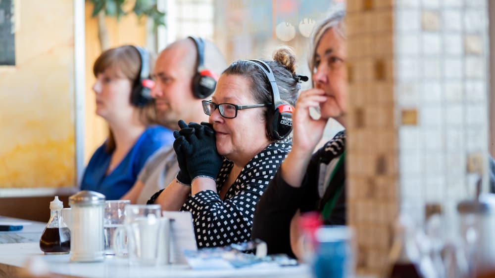 Women and men sitting in a cafe with headphones on.