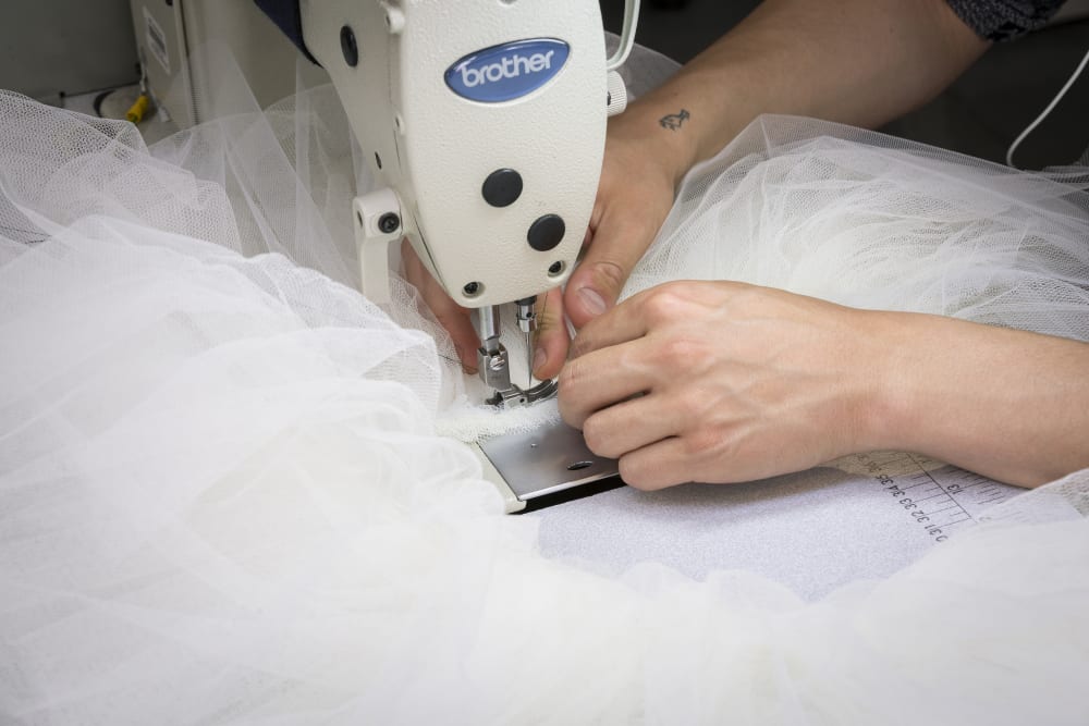 Close up of hands using a brother sewing machine on white tulle