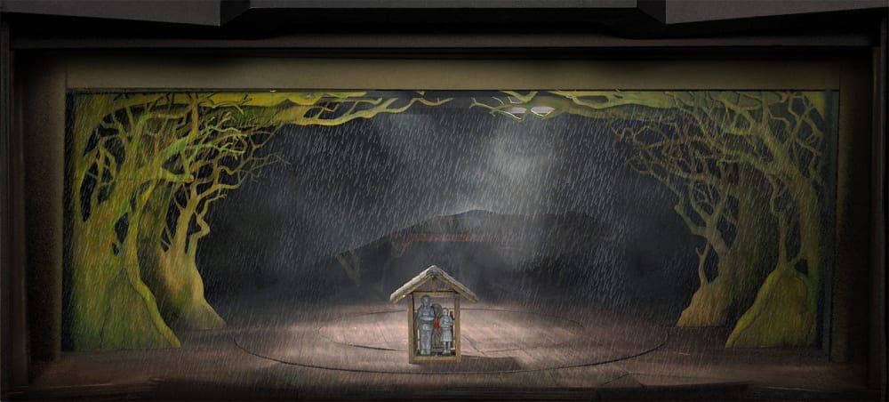 Image shows a model box of a stage with greenery around the perimeter and 2 people standing under a shelter in the centre of the stage