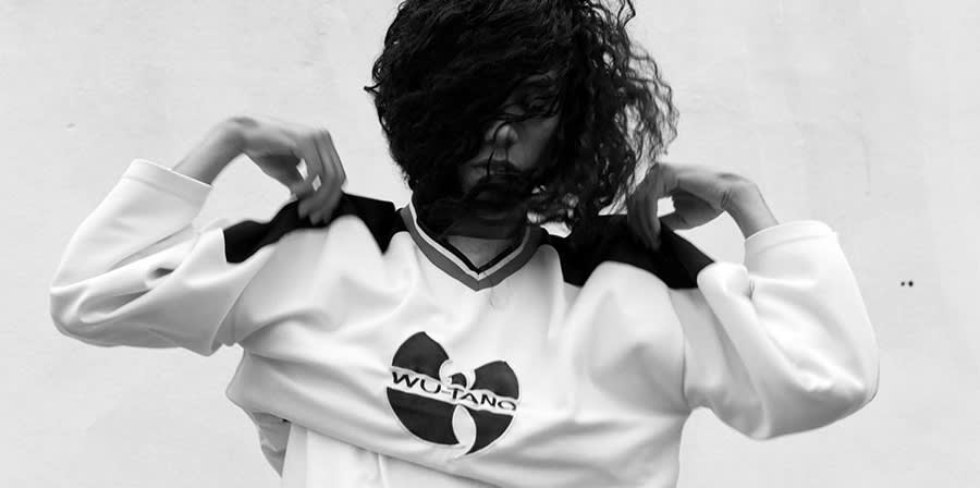 A young man taking of a sweat shirt with a 'Wu-Tang' logo