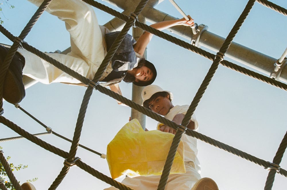 Two people stood on a climbing frame in tonal clothes. They are looking down at the camera