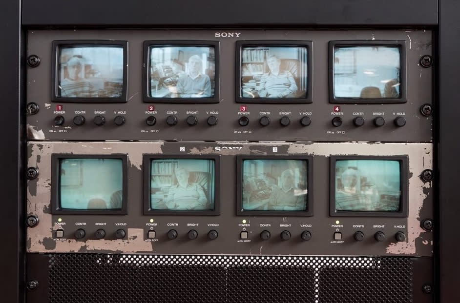 A close up of 2 vintage-looking Sony TV monitor racks. Each rack has four small screens which display images of individual people sitting down.