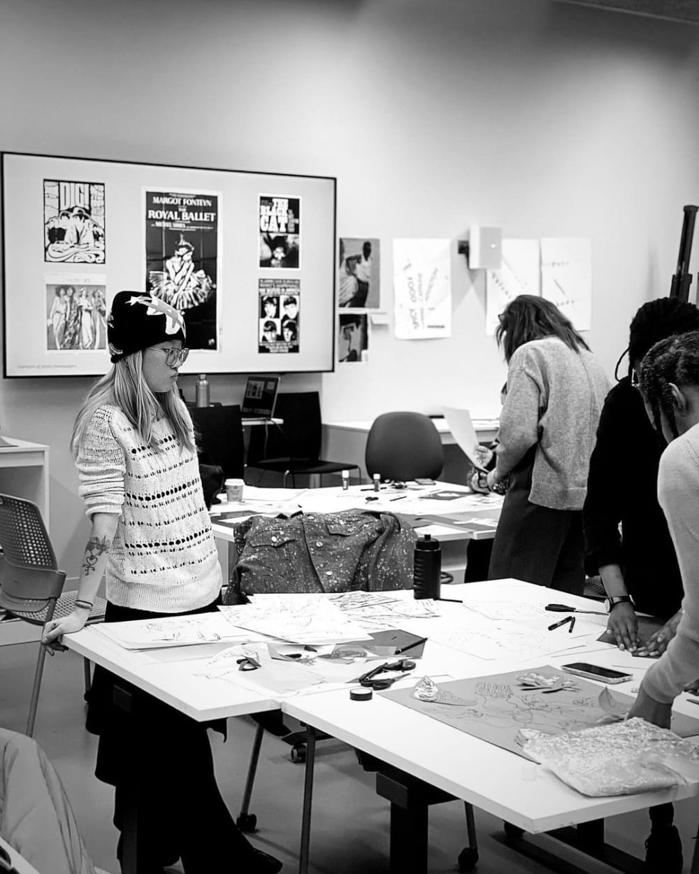 Person leaning on table with drawings on it, in classroom.