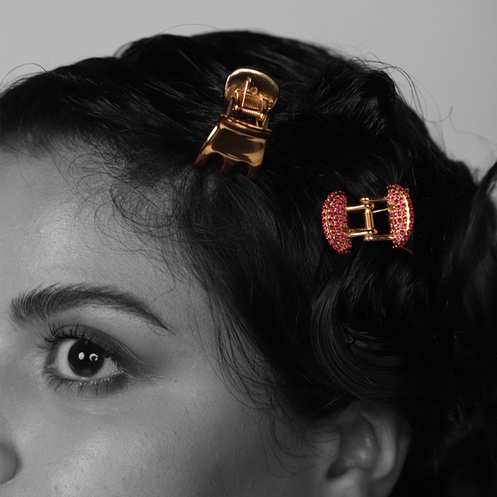 Black and white photo of a models hair and forehead. Her hair is pinned back by 2 butterfly clips which are in colour; gold with red rubies covering them