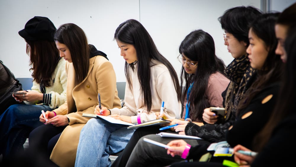 People sitting on chairs writing on pieces of paper.