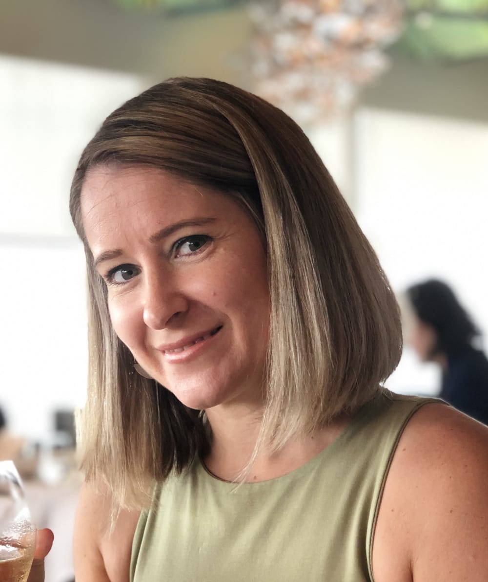 Headshot of Gemma, she has blonde hair in a long, straight bob style. She's wearing a sage green sleeveless top and she's smiling into the camera.